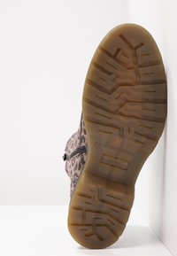 Suela de una bota de tobillo con estampado de leopardo, con una suela marrón translúcida, mirando hacia adelante sobre un fondo blanco.