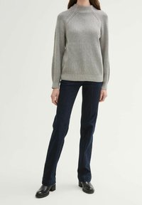 Grijze geribbelde gebreide trui met een hoge kraag, gecombineerd met donkerblauwe slim-fit jeans en zwarte enkellaarzen. Textuurstof en een aansluitend ontwerp.