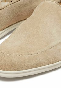 Beige suede loafers with a smooth texture, round toe, and white rubber sole. Subtle stitching details enhance the minimalist design.