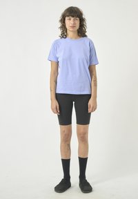 Helllila Baumwoll-T-Shirt mit kurzen Ärmeln, kombiniert mit schwarzen Radhosen, schwarzen knielangen Socken und schwarzen Schuhen. Einfaches Design, ohne Muster.
