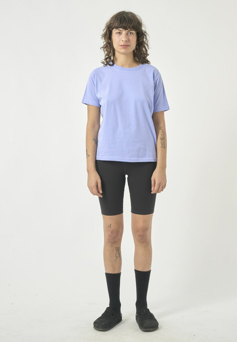 Helllila Baumwoll-T-Shirt mit kurzen Ärmeln, kombiniert mit schwarzen Radhosen, schwarzen knielangen Socken und schwarzen Schuhen. Einfaches Design, ohne Muster.