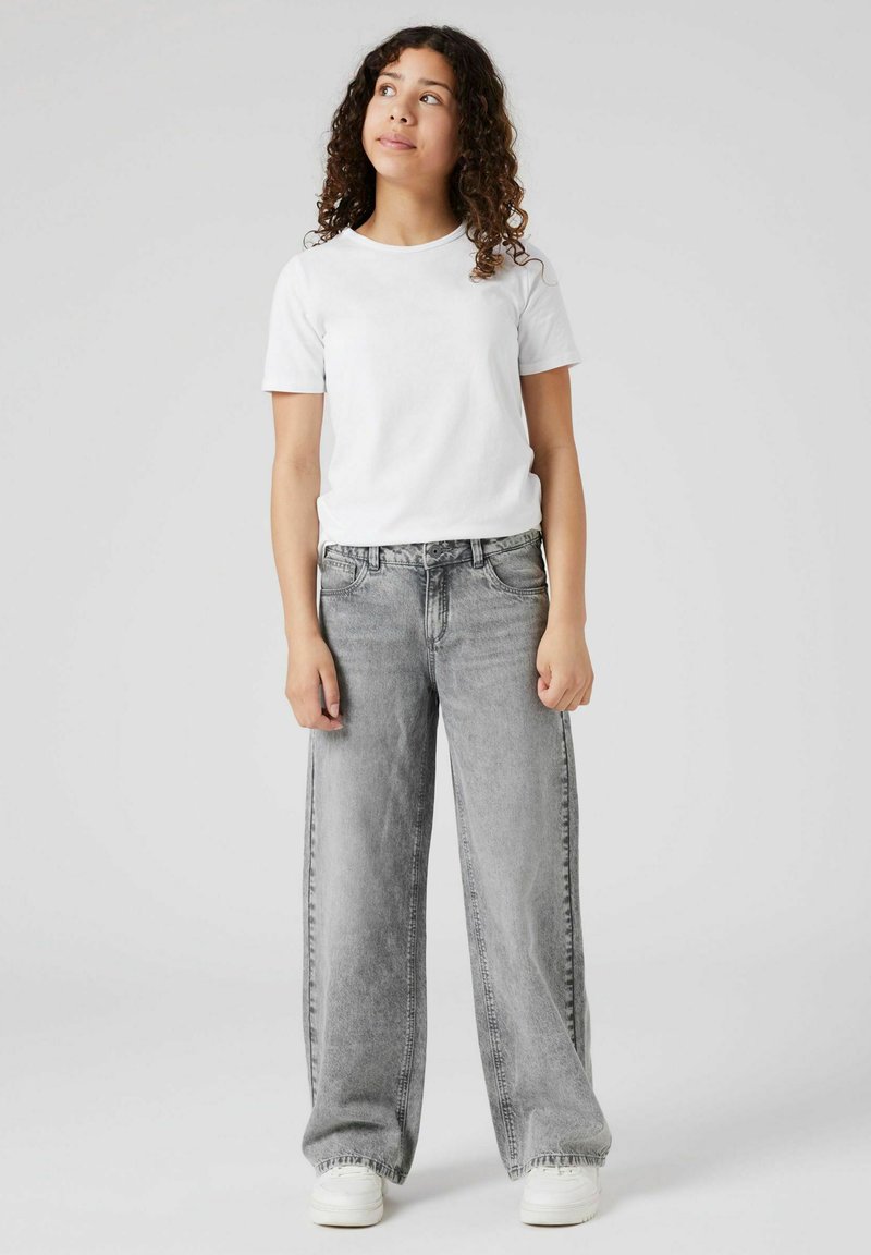 Jeans gri cu picioare largi, cu o finisare uzată, asortați cu un tricou alb simplu cu mânecă scurtă și adidași albi. Design simplu, fără modele.