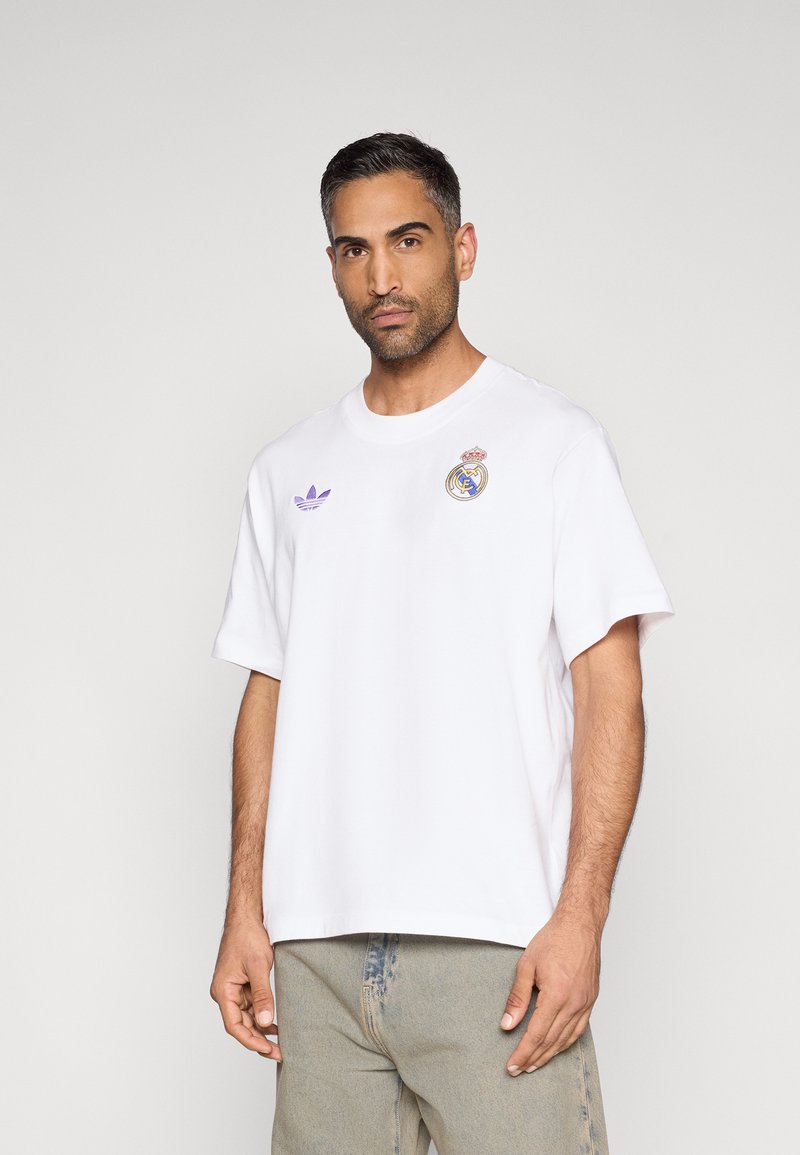 T-shirt branca de manga curta feita de algodão. Apresenta o logótipo roxo da Adidas e o emblema do Real Madrid no peito. Corte casual e descontraído.
