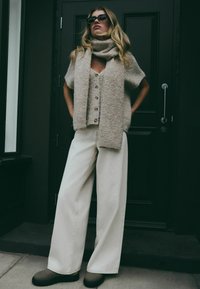 Beżowy krótkie sweter dziergany z zapięciem na guziki, w połączeniu z off-white szerokimi spodniami i ciemnym obuwiem, uzupełniony pasującym szalikiem.
