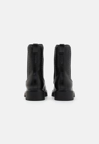 Botas de cuero negras hasta el tobillo con acentos de tachuelas, tacones resistentes y tiradores; textura suave con líneas limpias y un diseño minimalista.
