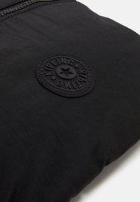 Borsa Kipling nera in tessuto nylon testurizzato, con una patch rotonda in gomma con il logo e una chiusura con zip lungo il bordo superiore.