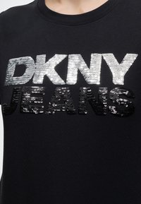 Μαύρο T-shirt με ασημί παγιέτες γράμματα "DKNY" και μαύρα γράμματα με παγιέτες που σχηματίζουν "JEANS" στο στήθος.