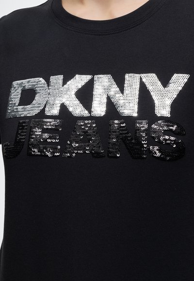 Черна тениска с сребристи букви с пайети "DKNY" и черни букви с пайети, изписващи "JEANS" на гърдите.