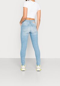 Jeans skinny de color azul claro con una cintura alta, diseño de cinco bolsillo y detalles de desvanecimiento. Combinados con un top corto blanco y zapatillas blancas.
