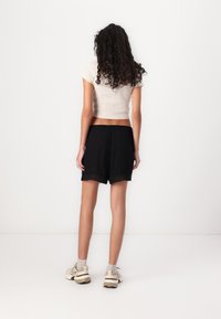 Shorts neri con pizzo, abbinati a un top corto di un beige chiaro. La vista frontale mostra una vestibilità rilassata e una consistenza morbida, indossati con sneakers.