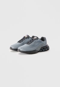 Chaussures de sport grises avec une tige en maille, bout arrondi, accents noirs et une semelle texturée dotée d'éléments de rembourrage bien en évidence.