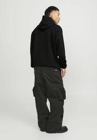 Sort hoodie med kængurulomme og snørehoed, kombineret med sorte cargobukser med flere sidelommer og en løs pasform.