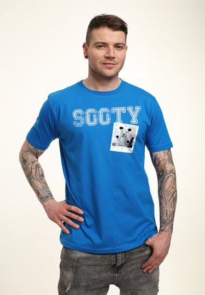 Blå bomulds t-shirt med "SOOTY" trykt i hvid, med en lomme-design og et sort-hvidt bjørne-graphic. Omfatter korte ærmer.