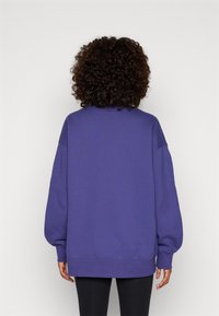 Sudadera morada de gran tamaño con mangas largas, puños y dobladillo acanalados. Textura suave, con un cuello redondo y diseño de hombros caídos.