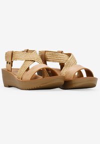 Las sandalias de cuña marrones presentan correas trenzadas en tono arena, una plantilla de cuero suave y una suela de goma texturizada con un ligero patrón de agarre.