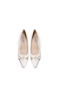 Scarpe bianche in pelle con punta allungata e texture liscia, dotate di un dettaglio a fibbia circolare dorata nella parte anteriore e di una soletta beige.