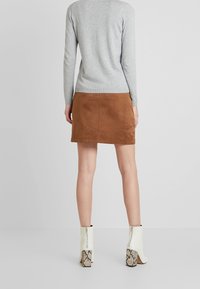 Suéter gris de manga larga combinado con una falda mini de ante marrón. El calzado incluye botas de tobillo de cuero blanco con tacones de estampado de serpiente.