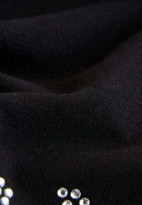 Črno blago z mehko teksturo, okrašeno s prozornimi kristalčki, ki tvorijo vzorec. Poudarek je na gladkosti in detajlih.