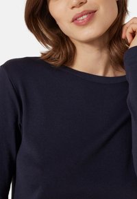 Marineblaues Langarmshirt mit Rundhalsausschnitt und glatter Textur. Nahtdetails sind in der Nähe von Kragen, Ärmeln und Saum sichtbar.