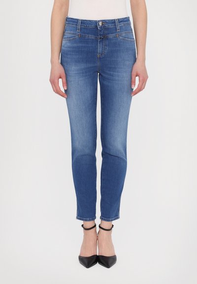 Blaue Jeans aus Denim mit figurbetontem Schnitt, mittelhohem Bund und leicht ausgefranstem Saum. Kombiniert mit schwarzen spitzen Pumps.