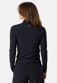 Svart långärmad topp med ribbat mönster, hög hals och en guldlogotyp på baksidan. Har en ficka med dragkedja vid midjan.