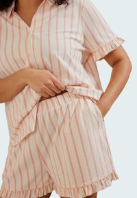 Ensemble de pyjama en coton léger avec des rayures roses et blanches. Le haut à boutons présente des manches courtes à volants ; le bas a une taille élastique et un ourlet à volants.