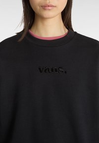 Sweatshirt noir avec un col rond et un logo "vans." brodé. Superposé avec une chemise rose en dessous. Texture de matériau douce.