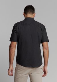Korte mouw zwarte shirt, gemaakt van lichtgewicht stof, heeft een kraag, een knoop aan de achterkant en een rechte zoom. Eenvoudig ontwerp, geen patronen.