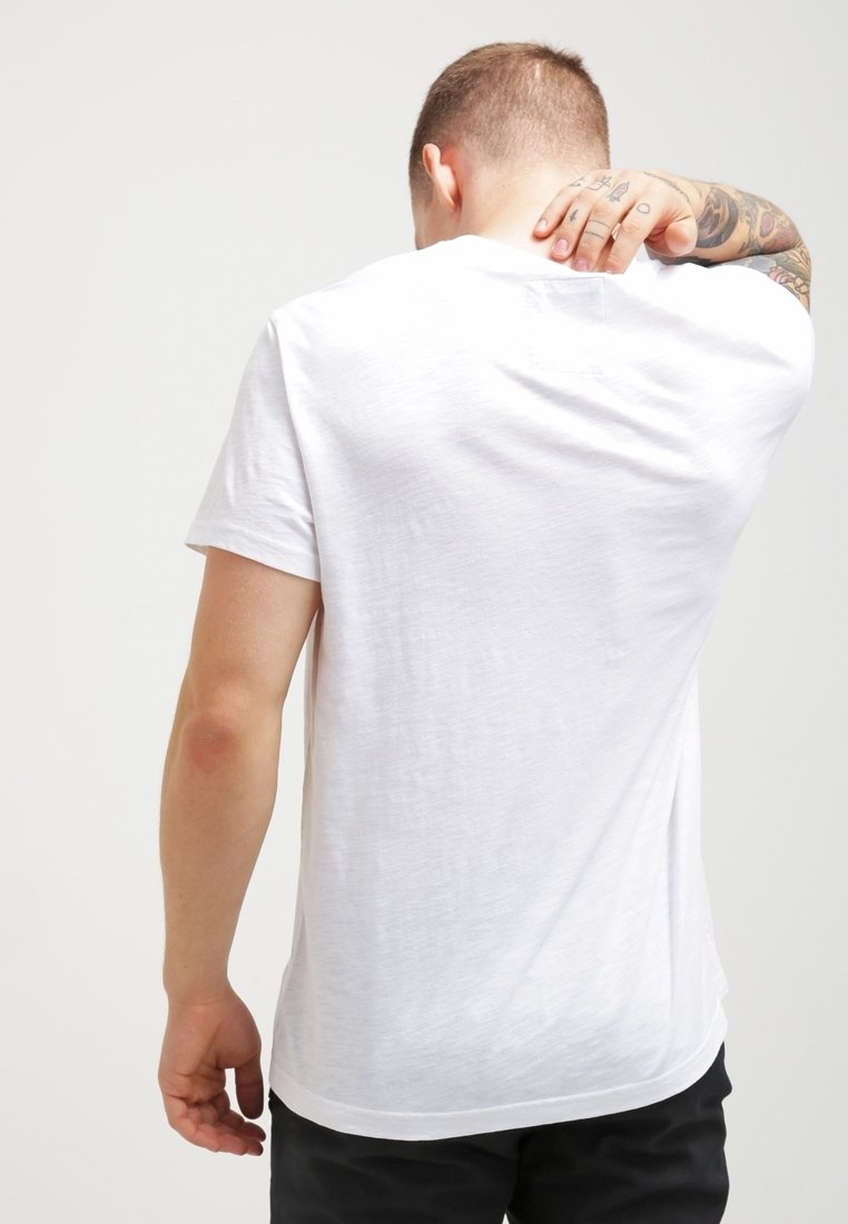 Vit kortärmad t-shirt i mjuk, texturerad tyg, rund halsringning och bågformad kant. Har en enkel baksida utan grafik.