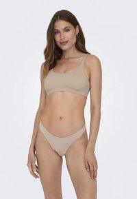 Béžová žebrovaná braletka se širokými ramínky, v kombinaci s odpovídající minimalistickou tangou. Hladká textura a přiléhavý střih pro pohodlí.