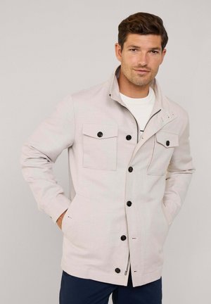 Hellgraue Jacke aus strukturiertem Stoff. Verfügt über einen Stehkragen, vier Fronttaschen und schwarze Knöpfe. Reißverschluss am Saum.