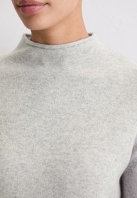 Grijze trui met een hoge hals, gemaakt van zachte, gestructureerde stof; heeft een lichte gemêleerde afwerking en een nauwsluitend ontwerp.