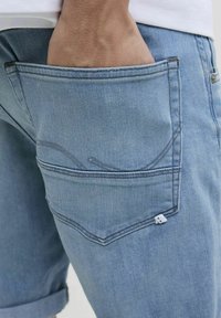 Lyseblå denimshorts med opsmøg, der har en baglomme med buet søm og et lille mærke i nederste hjørne.