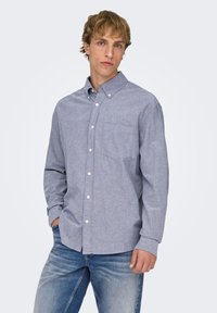 Lyseblå skjorte med knapper lavet af blødt stof, med en enkelt brystlomme, lange ærmer og design med krave.