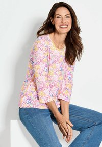 Lichtgewicht, top met bloemenpatroon in roze, geel en paarse tinten, met driekwartmouwen en een ronde halslijn, in combinatie met blauwe jeans.