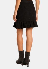 Jupe noire en tricot avec un motif texturé et un ourlet froncé, associée à des bottines noires élégantes.
