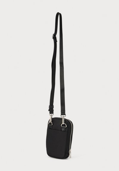 Black crossbody bag made of smooth fabric, featuring a front pocket and silver hardware, with an adjustable strap and zip closure.