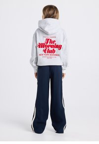 Gray hoodie with a large red graphic on the back, featuring text; paired with navy blue wide-leg pants with white side stripes.