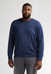 Marineblauwe langharige trui met een ronde hals, zachte textuur en geribbelde manchetten, gecombineerd met grijze jeans. Eenvoudig, effen ontwerp.