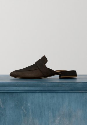 Scarpa mule in pelle nera slip-on con tacco basso a blocchetto, appoggiata su una superficie di legno blu contro uno sfondo semplice.