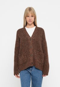 Brązowy sweter kardigan z dekoltem w kształcie V, z przodem na guziki i dwoma przednimi kieszeniami. Charakteryzuje się teksturowanym wzorem i luźnym fasonem.