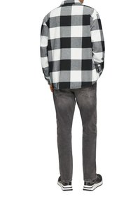 Zwart-wit geruite flanellen shirt met lange mouwen van zachte stof. Draagt het met donkergrijze broek en zwarte sneakers met witte accenten.