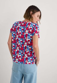 Camiseta de manga corta en azul, rojo y blanco con un patrón de círculos y rayas. Tejido suave con un corte relajado, que presenta un escote redondeado.