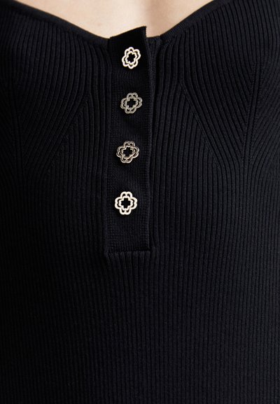 Top negru cu o textură ribbed, având un decolteu în formă de V și nasturi decorativi cu design floral. Stoffa are un aspect texturat și ajustat.