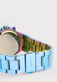 Reloj de acero inoxidable con acabado pulido en colores arcoíris, que cuenta con una corona texturizada y un cierre seguro. La parte trasera está grabada con los detalles de la marca.