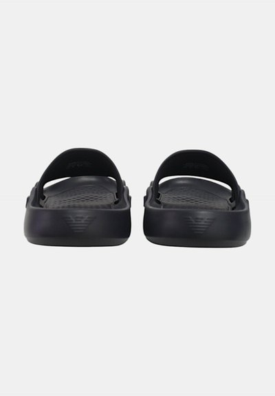 Černé pantofle s plochou podrážkou, zakřivenými pásky a texturovanou stélkou s logem a větraným designem. Hladký plastový materiál.