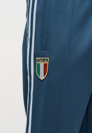 Kék sportnadrág fehér oldalsávokkal és egy Italia jelvénnyel, amely zöld, fehér és piros függőleges csíkokat ábrázol.