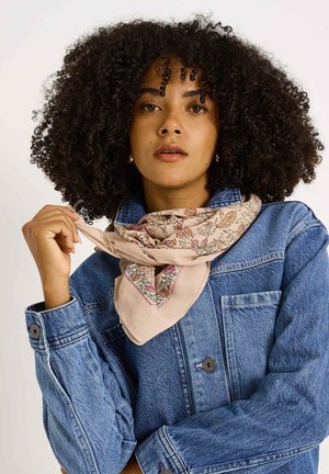 Bufanda de color rosa claro con estampado floral, colocada alrededor del cuello, combinada con una chaqueta de mezclilla que tiene puños con botones y bolsillo en el pecho.