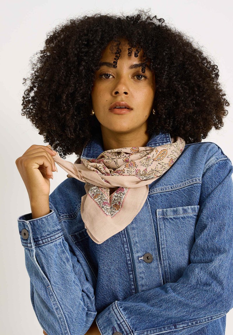 Bufanda de color rosa claro con estampado floral, colocada alrededor del cuello, combinada con una chaqueta de mezclilla que tiene puños con botones y bolsillo en el pecho.