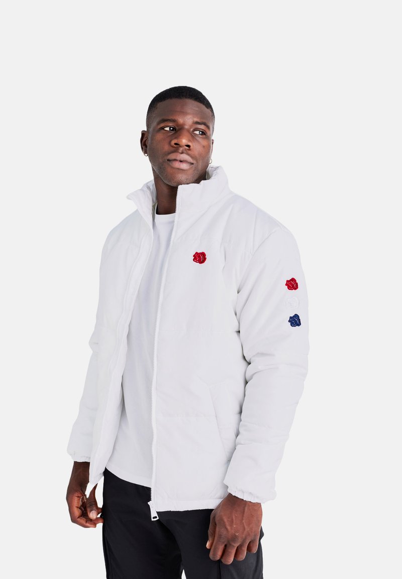 Giacca bianca imbottita con colletto alto, zipper frontale e tasche frontali. Presenta accenti floreali ricamati in rosso e blu sulle maniche.
